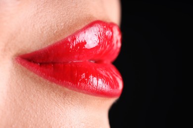 Photo of Woman with beautiful red lipstick on her lips against black background, macro view. Space for text