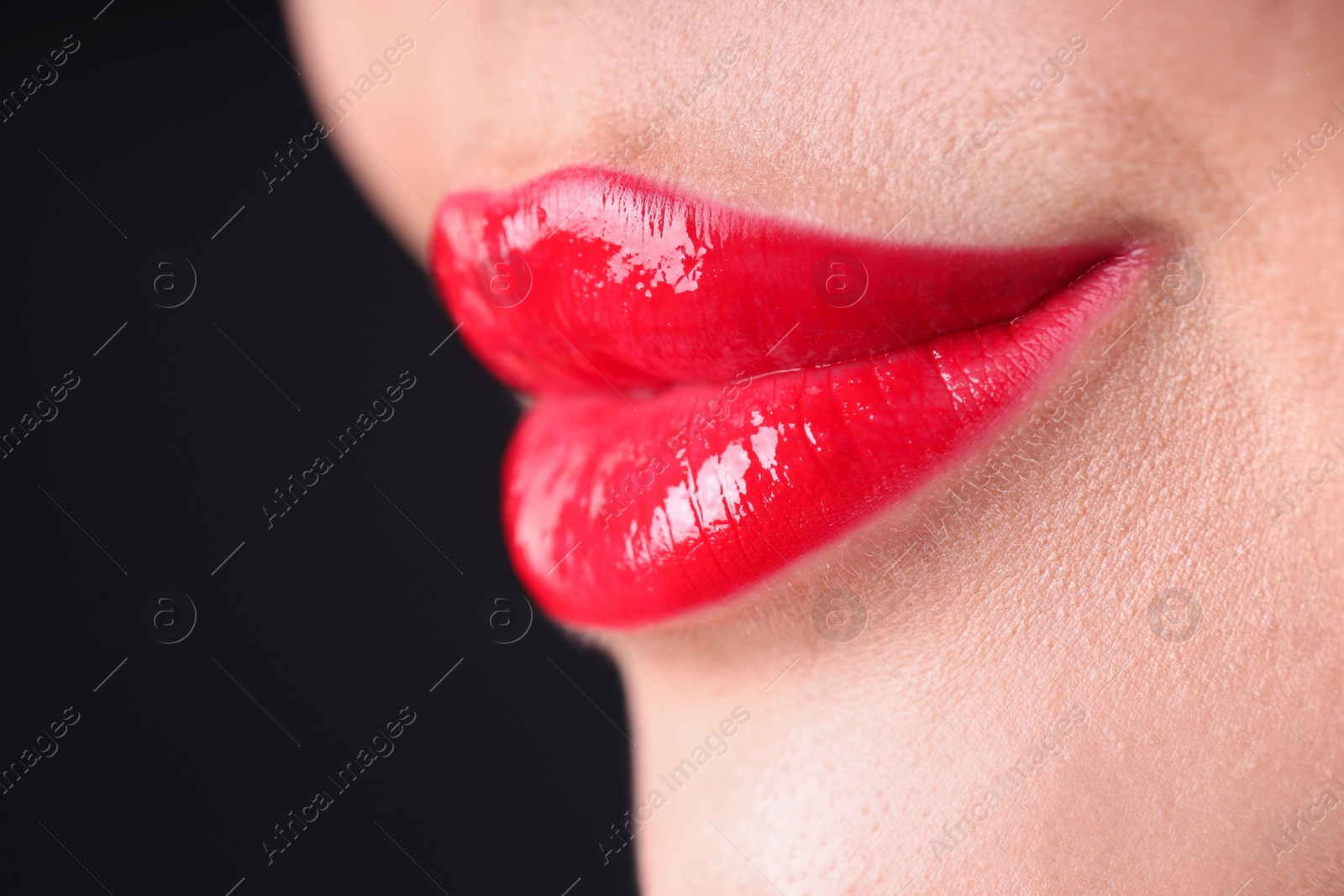 Photo of Woman with beautiful red lipstick on her lips against black background, macro view. Space for text