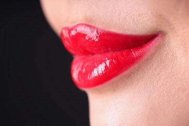 Photo of Woman with beautiful red lipstick on her lips against black background, macro view. Space for text
