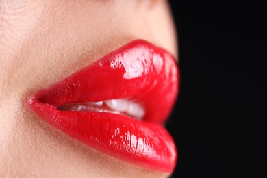 Photo of Woman with beautiful red lipstick on her lips against black background, macro view. Space for text