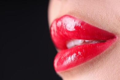 Photo of Woman with beautiful red lipstick on her lips against black background, macro view. Space for text