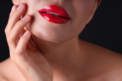 Photo of Woman with beautiful red lipstick on her lips against black background, macro view