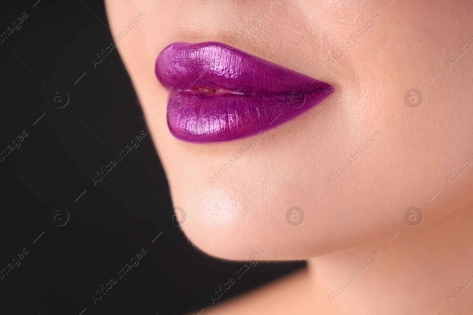 Photo of Woman with beautiful purple lipstick on her lips against black background, macro view