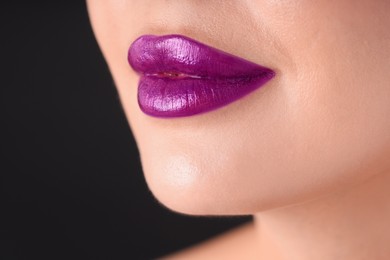Photo of Woman with beautiful purple lipstick on her lips against black background, macro view