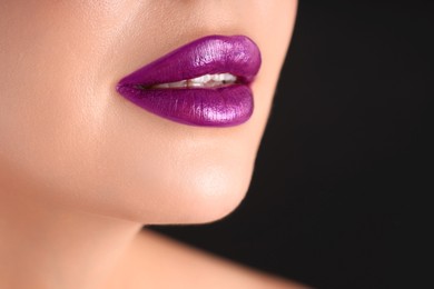 Photo of Woman with beautiful purple lipstick on her lips against black background, macro view
