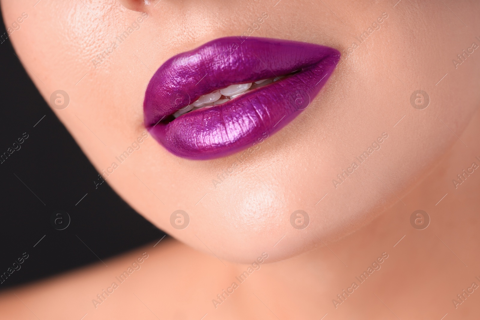 Photo of Woman with beautiful purple lipstick on her lips against black background, macro view