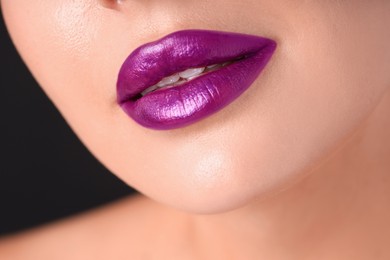 Photo of Woman with beautiful purple lipstick on her lips against black background, macro view