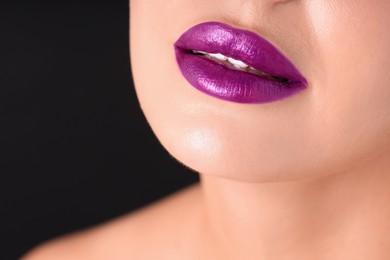 Photo of Woman with beautiful purple lipstick on her lips against black background, macro view