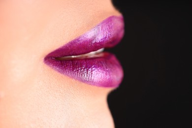Photo of Woman with beautiful purple lipstick on her lips against black background, macro view. Space for text