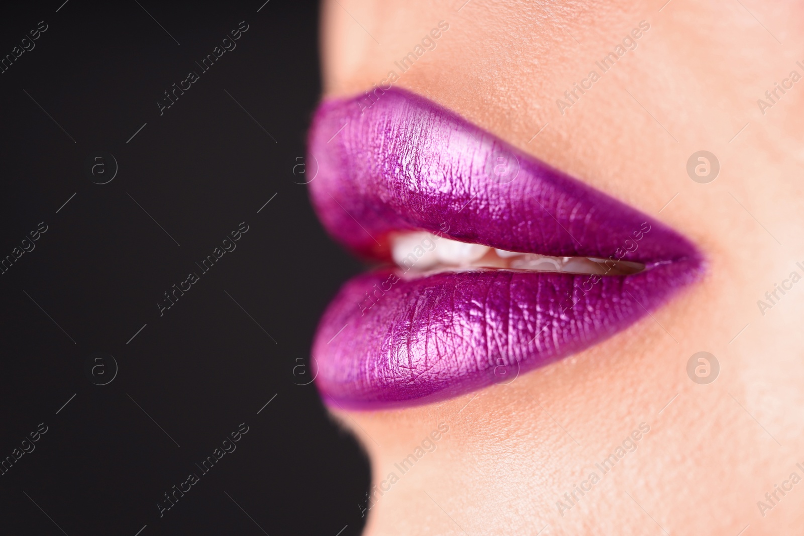 Photo of Woman with beautiful purple lipstick on her lips against black background, macro view. Space for text