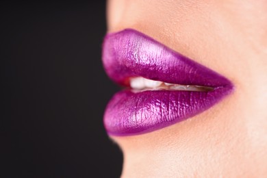 Photo of Woman with beautiful purple lipstick on her lips against black background, macro view. Space for text