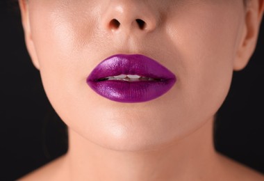 Photo of Woman with beautiful purple lipstick on her lips against black background, macro view