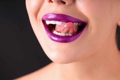 Photo of Woman with beautiful purple lipstick on her lips against black background, macro view