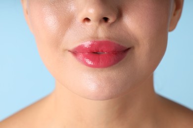 Photo of Woman with beautiful pink lipstick on her lips against light blue background, macro view