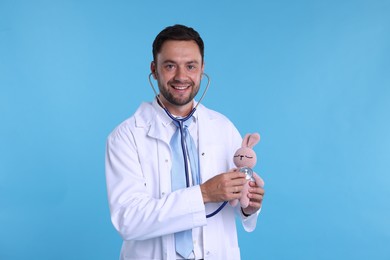 Photo of Pediatrician checking heartbeat of toy bunny on light blue background