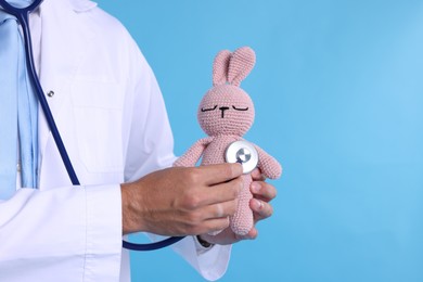 Photo of Pediatrician checking heartbeat of toy bunny on light blue background, closeup. Space for text