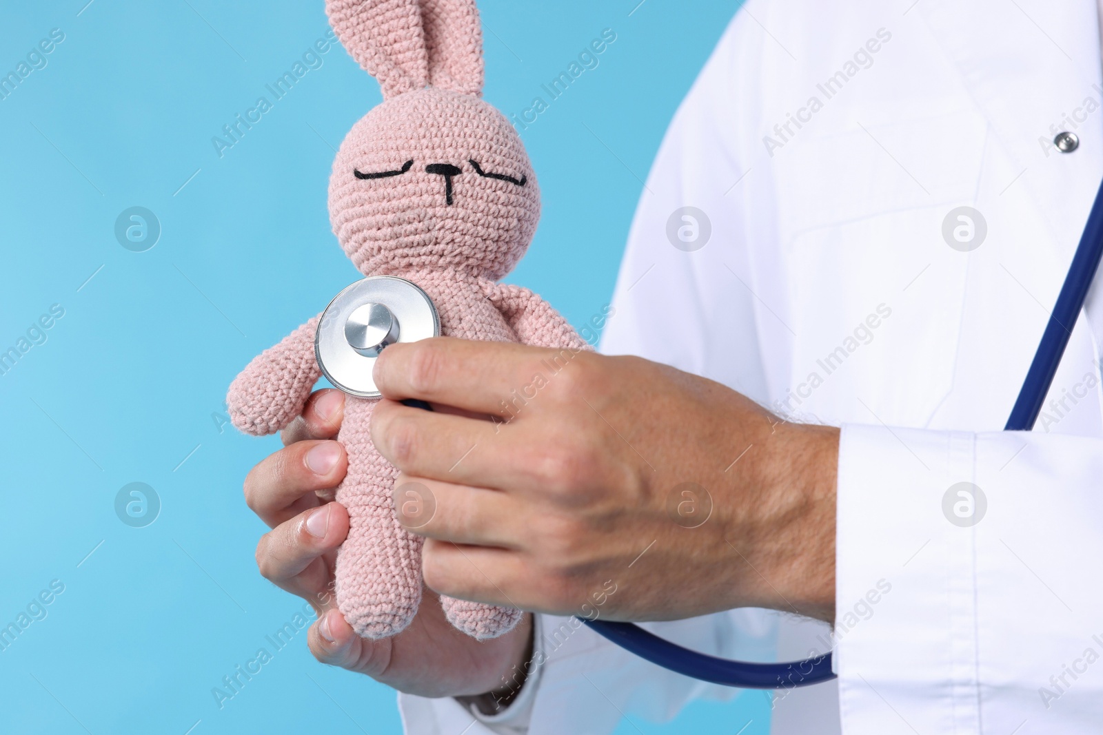 Pediatrician checking heartbeat of toy bunny on light blue background, closeup Photo of Pediatrician checking heartbeat of toy bunny on light blue background, closeup