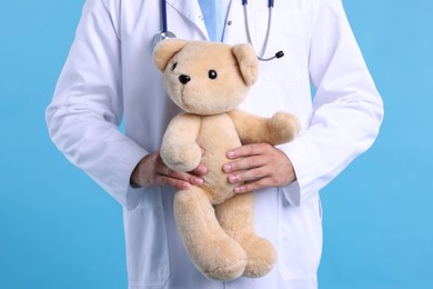 Photo of Pediatrician with teddy bear on light blue background, closeup