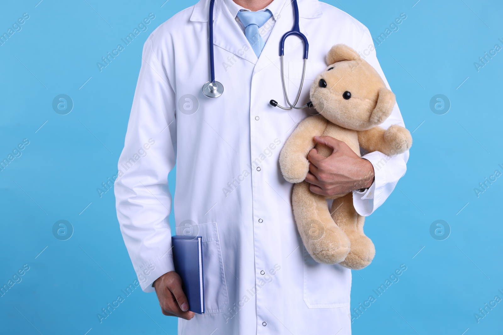 Photo of Pediatrician with teddy bear and notebook on light blue background, closeup
