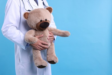 Photo of Pediatrician with teddy bear on light blue background, closeup. Space for text