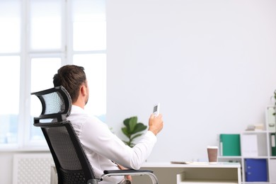 Photo of Man using remote to control air conditioner in office, back view