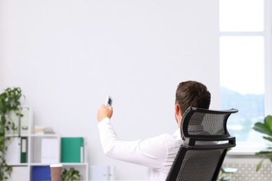 Photo of Man using remote to control air conditioner in office, back view