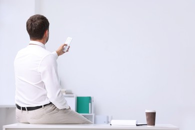 Photo of Man using remote to control air conditioner in office, back view