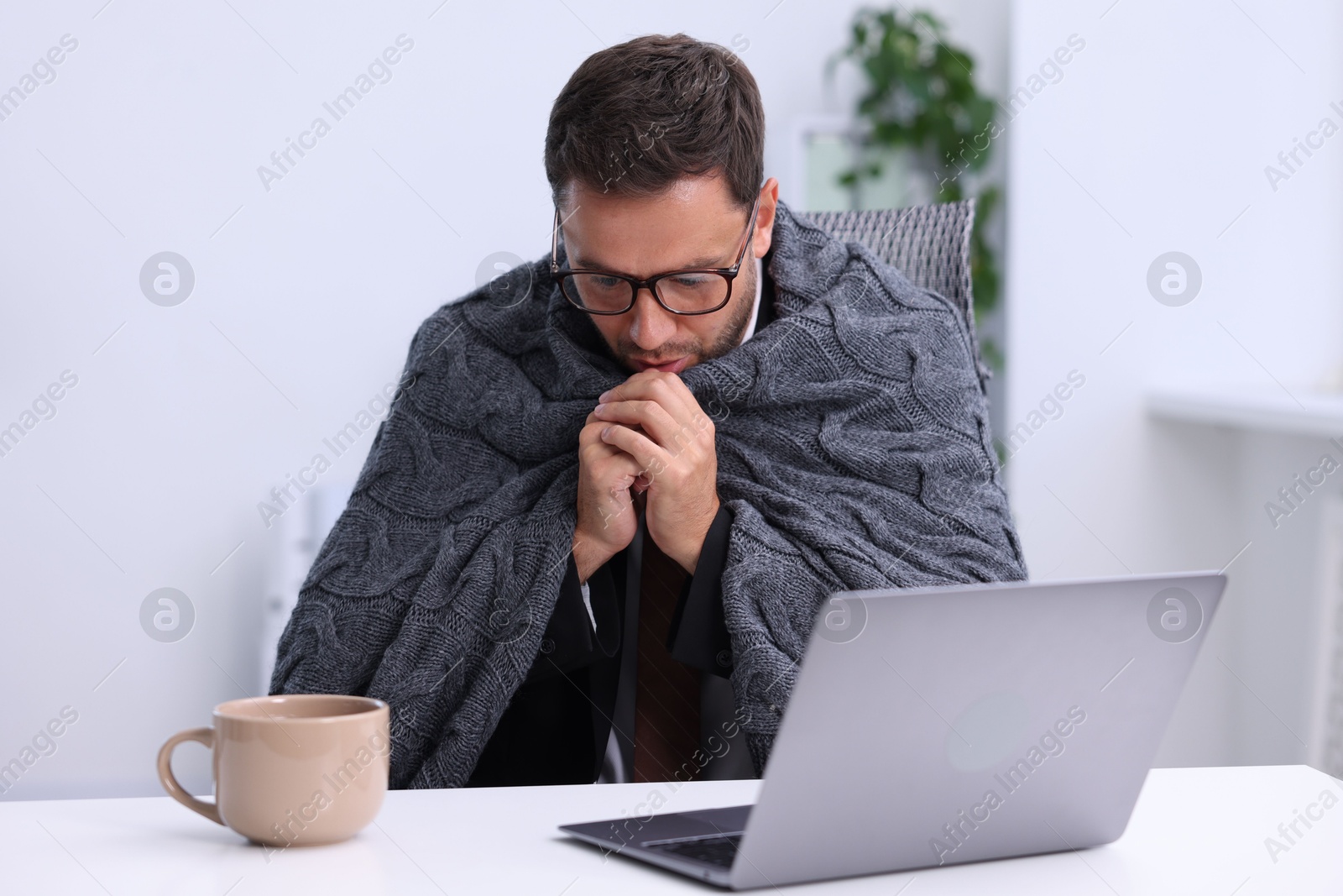 Photo of Air conditioning. Man with blanket suffering from cold temperature at workplace in office