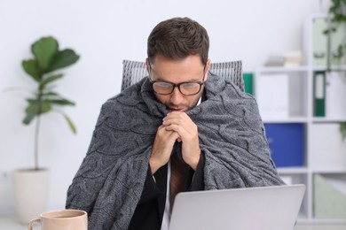 Photo of Air conditioning. Man with blanket suffering from cold temperature at workplace in office
