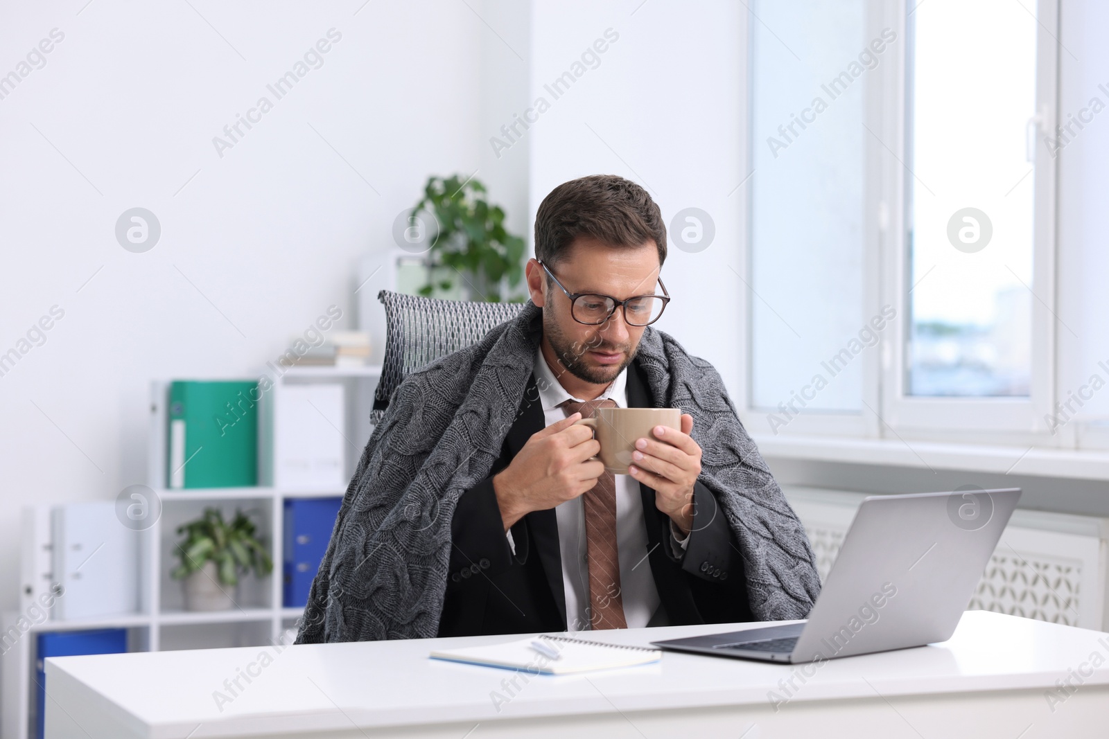 Photo of Air conditioning. Man with cup of hot drink suffering from cold temperature at workplace in office