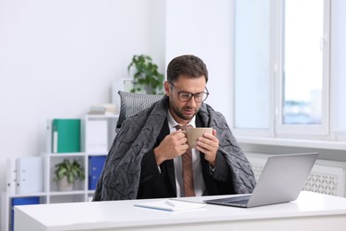 Photo of Air conditioning. Man with cup of hot drink suffering from cold temperature at workplace in office