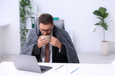 Photo of Air conditioning. Man with cup of hot drink suffering from cold temperature at workplace in office