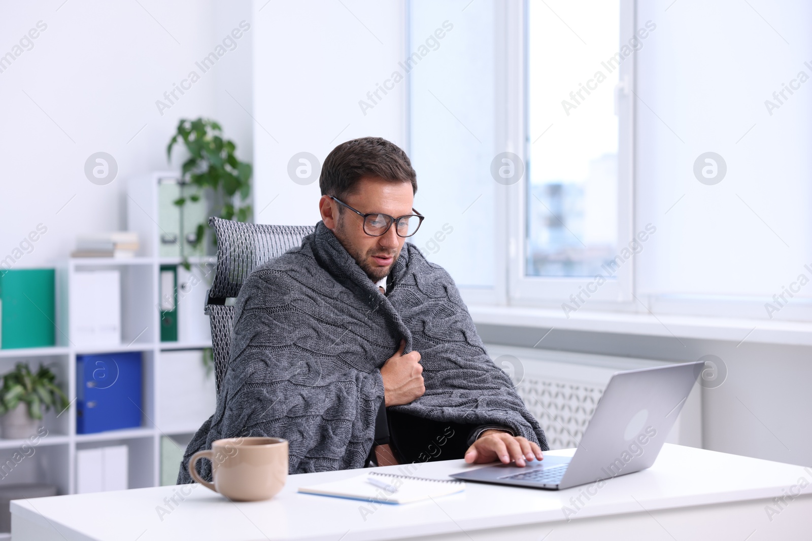 Photo of Air conditioning. Man with blanket suffering from cold temperature at workplace in office