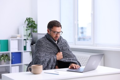 Photo of Air conditioning. Man with blanket suffering from cold temperature at workplace in office