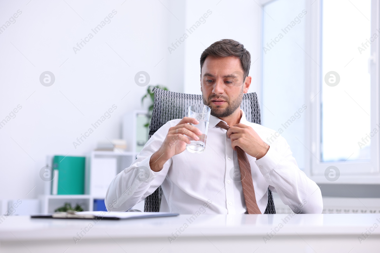 Photo of Air conditioning. Man with glass of water suffering from heat at workplace in office