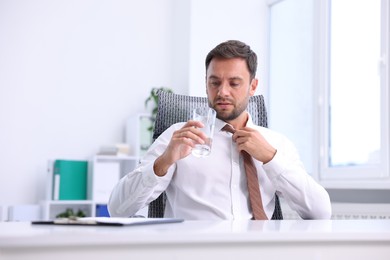 Photo of Air conditioning. Man with glass of water suffering from heat at workplace in office