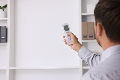 Photo of Man using remote to control air conditioner in office, back view