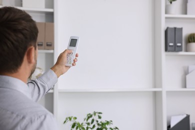 Photo of Man using remote to control air conditioner in office, back view