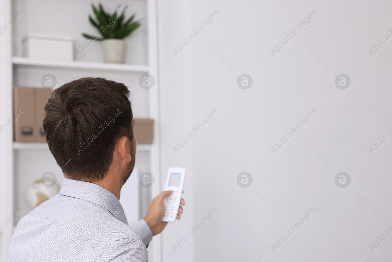 Photo of Man using remote to control air conditioner in office, back view