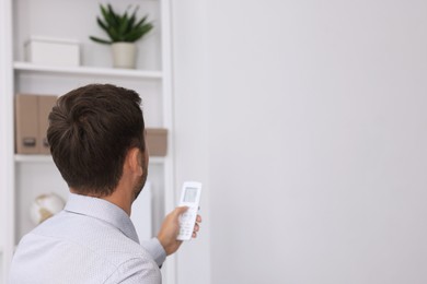 Photo of Man using remote to control air conditioner in office, back view