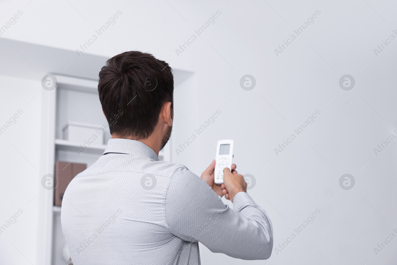 Photo of Man using remote to control air conditioner in office, back view
