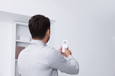 Photo of Man using remote to control air conditioner in office, back view