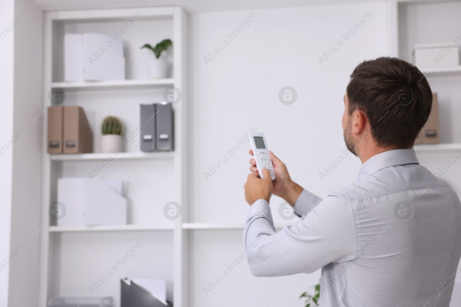 Photo of Man using remote to control air conditioner in office, back view