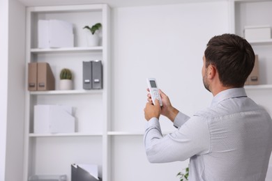 Photo of Man using remote to control air conditioner in office, back view