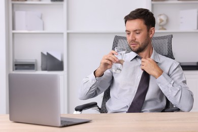 Photo of Air conditioning. Man with glass of water suffering from heat at workplace in office