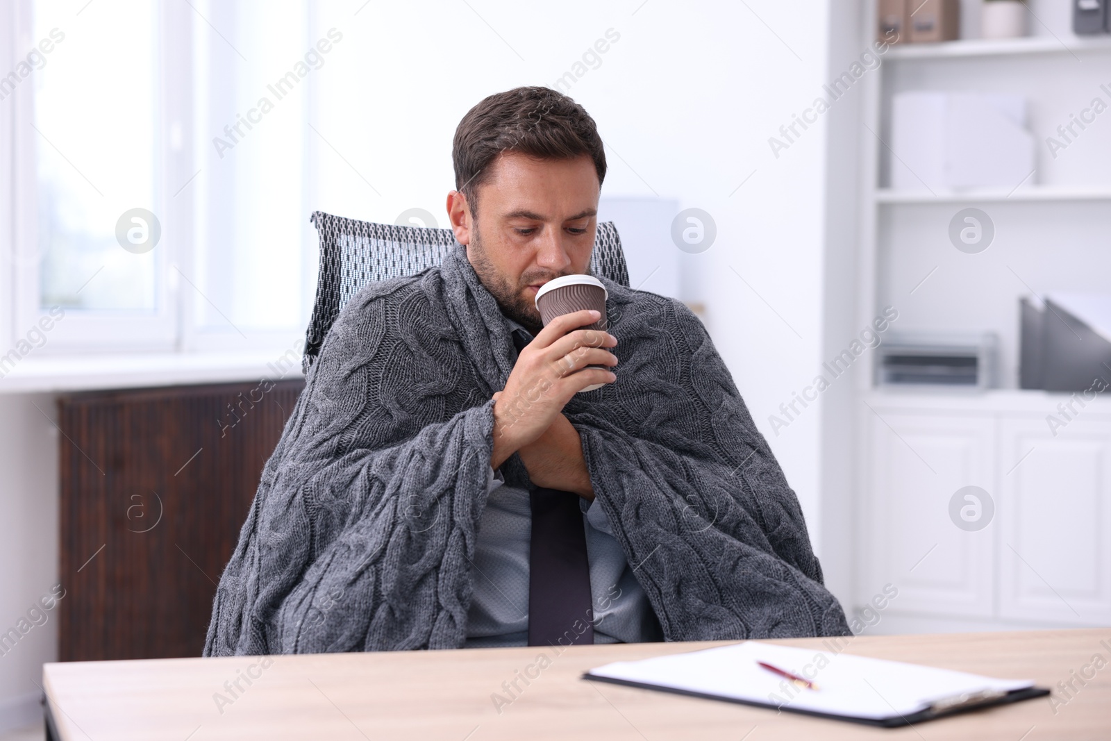 Photo of Air conditioning. Man with cup of hot drink suffering from cold temperature at workplace in office