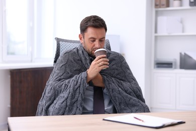 Photo of Air conditioning. Man with cup of hot drink suffering from cold temperature at workplace in office