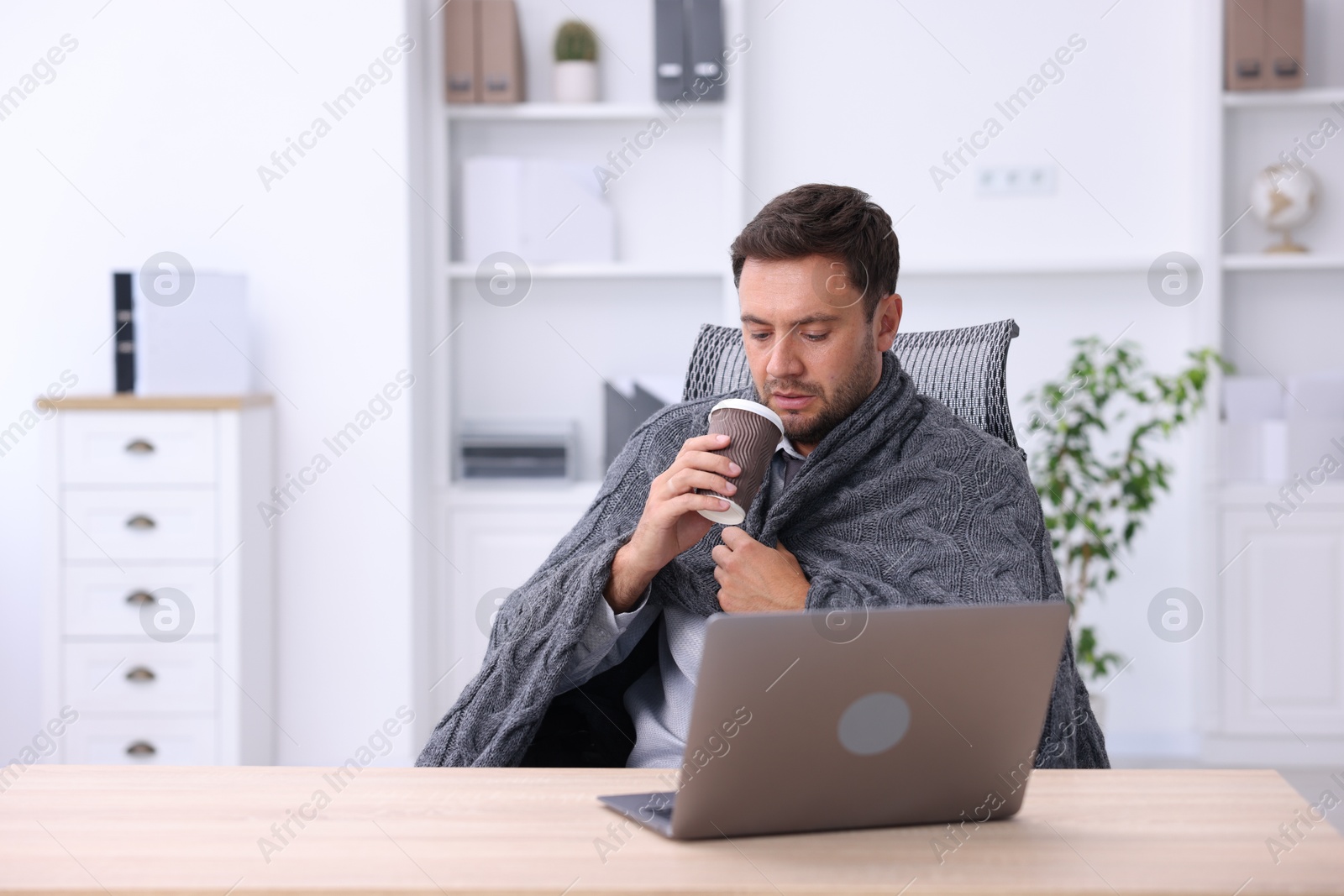 Photo of Air conditioning. Man with cup of hot drink suffering from cold temperature at workplace in office