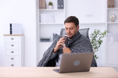 Photo of Air conditioning. Man with cup of hot drink suffering from cold temperature at workplace in office