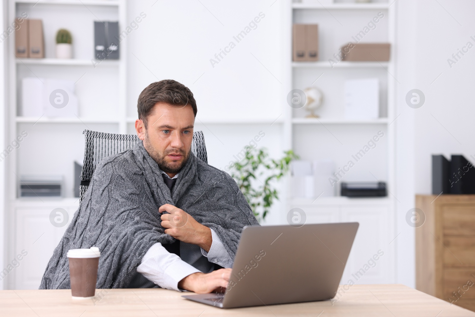 Photo of Air conditioning. Man with blanket suffering from cold temperature at workplace in office